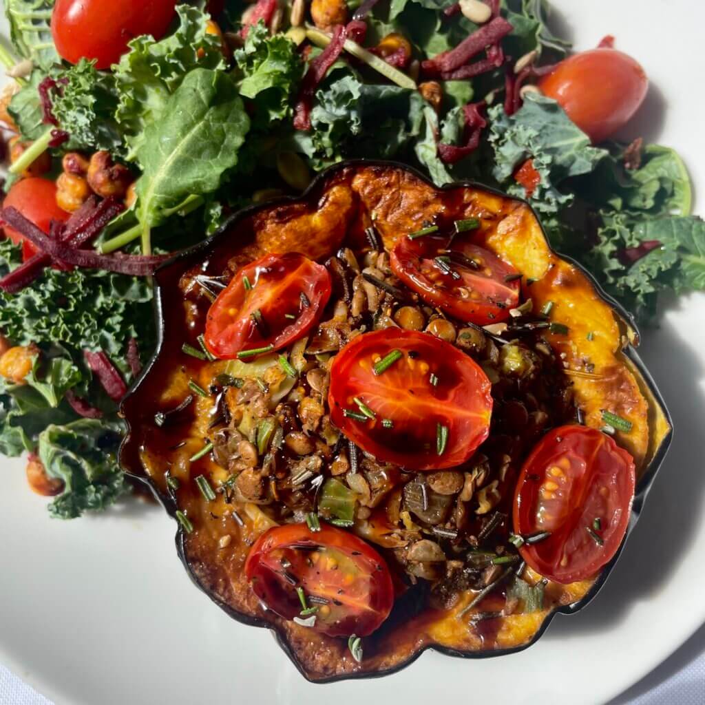 Acorn squash stuffed with lentils and spices topped with tomatoes and served with a side of greens.